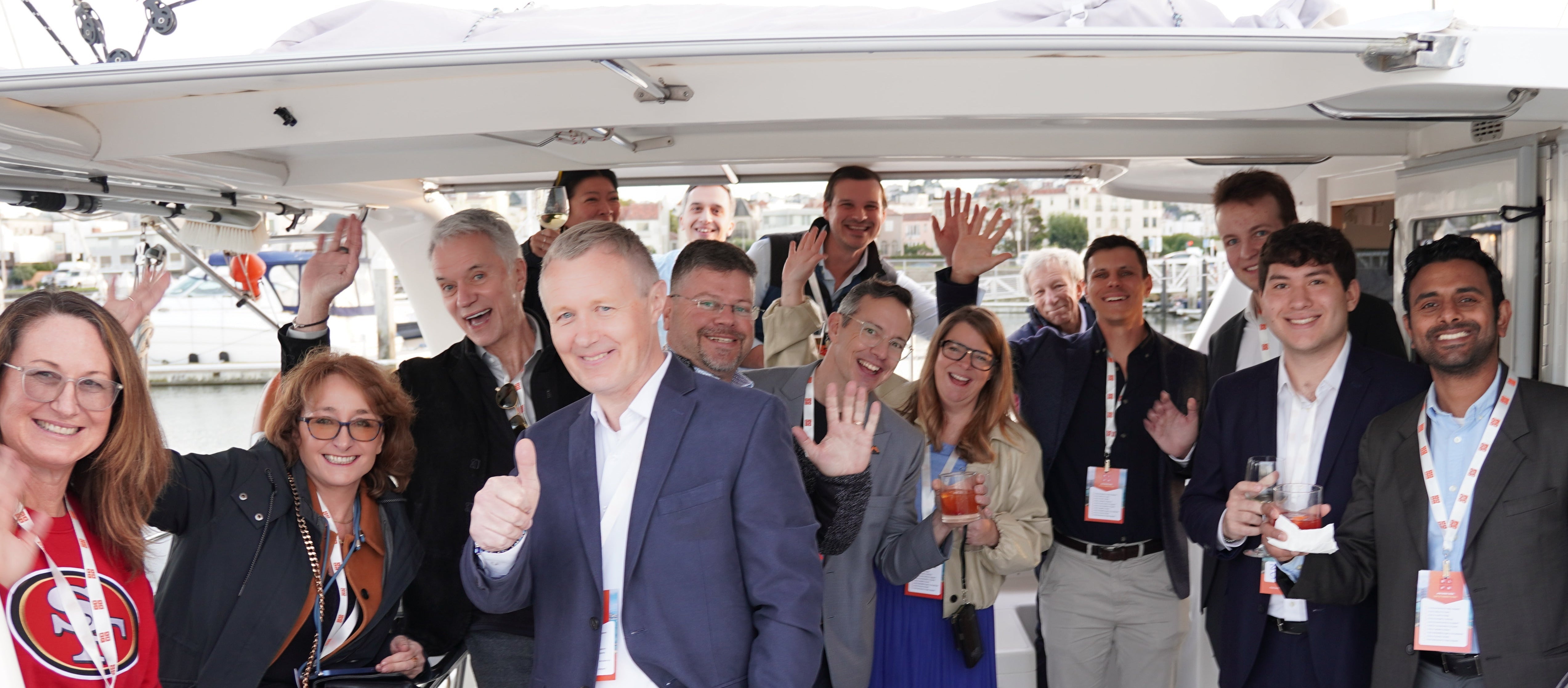 Group of people on a boat, some giving thumbs up, with a scenic background.